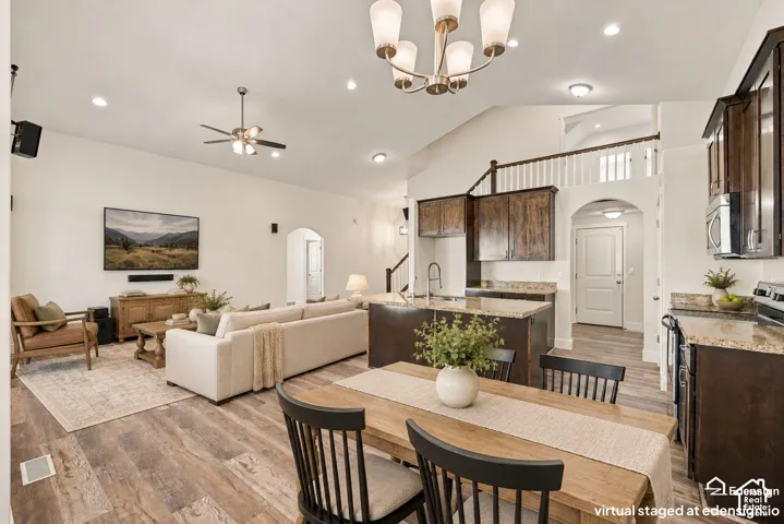 Vaulted ceilings with recessed lighting, wood-finish flooring, central kitchen island with stone-surface countertop, dark wood cabinetry, and a tiered architectural design featuring an upper-level mezzanine