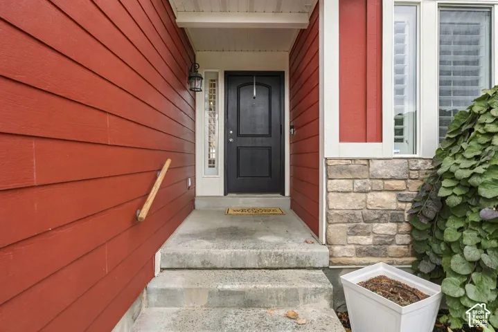 Covered entryway featuring horizontal lap siding, stone veneer accents, a solid-panel door with a sidelight, and an exterior wall-mounted lantern light