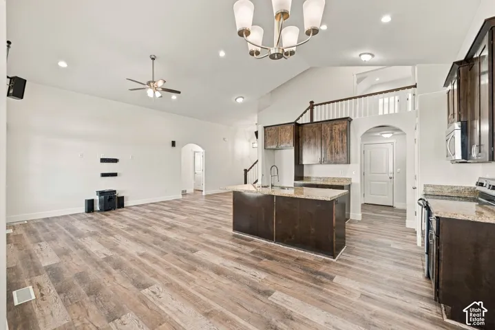 Open-concept space featuring vaulted ceilings, wood-finish flooring, a kitchen island with stone-surface countertops, dark wood cabinetry, and recessed lighting