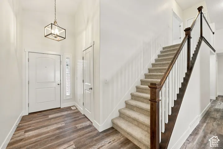 Entryway featuring high ceilings, wood-finish flooring, a pendant light fixture, and a staircase with carpeted treads and a wood-capped banister