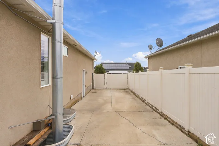 Side yard featuring concrete paving, a tall vinyl privacy fence, and a gate providing exterior access