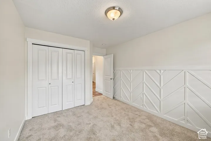 Interior room featuring chevron-pattern wall millwork, carpeted flooring, a four-panel bi-fold closet door, and a flush-mount ceiling light fixture