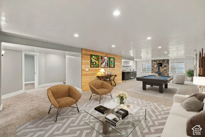 Open-concept interior featuring recessed lighting, a decorative natural wood plank accent wall, a floor-to-ceiling stone fireplace surround, and a built-in wet bar with dark cabinetry