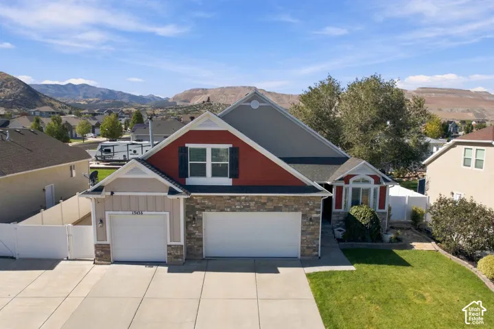 Multi-level exterior featuring stone veneer accents, lap and vertical siding, a three-car garage, and prominent mountain backdrop