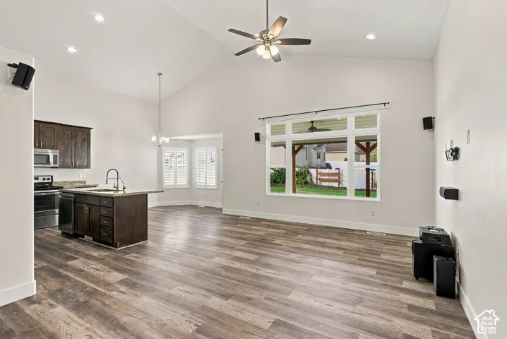 Open-concept interior featuring vaulted ceilings, wood-finish flooring, recessed lighting, stained wood cabinetry, and a large multi-pane window