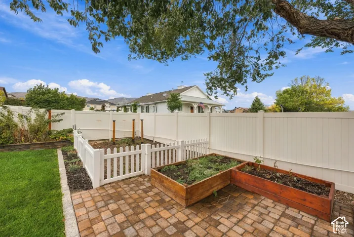 Private backyard featuring a full-height vinyl privacy fence, paver stone patio, raised wood garden beds, and a fenced-in garden area