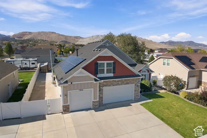 Exterior featuring a multi-material facade with stone veneer and vertical siding, roof-mounted solar panels, an attached two-car garage, and mountain scenery