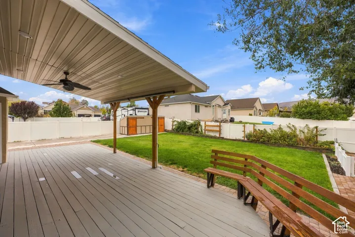Covered patio featuring a ceiling fan, composite decking, built-in wooden bench, lawn, and perimeter vinyl fencing