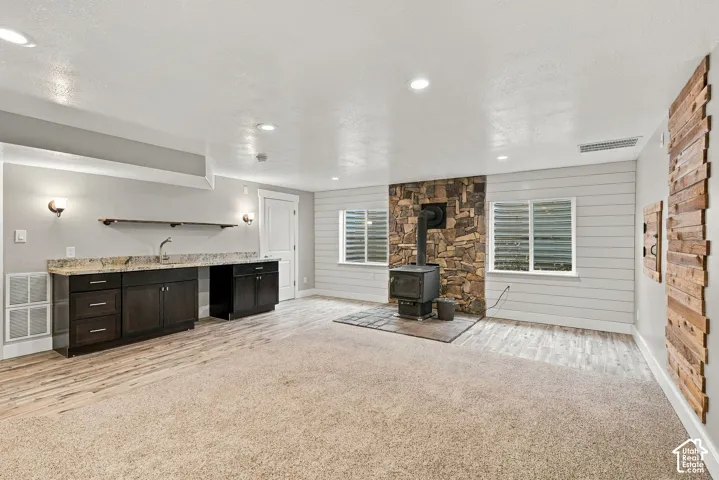 Stone-surround wood stove on a tile hearth, built-in wet bar with stone countertop, wood-plank wall accents, and recessed lighting