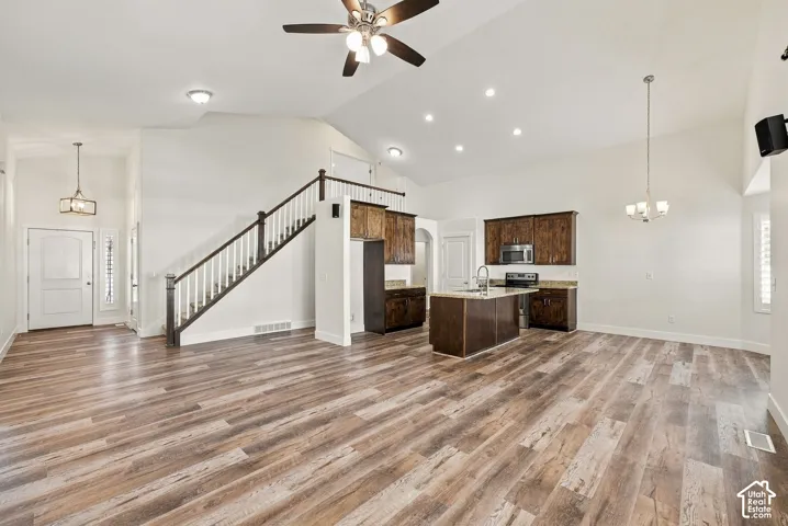 Open-concept living space featuring vaulted ceilings, wood-finish flooring, a kitchen island, recessed lighting, and a staircase with a wooden handrail