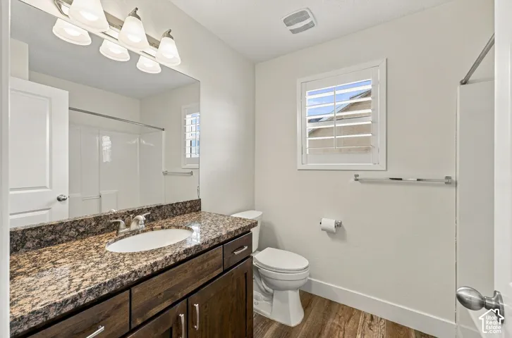 Bathroom featuring dark wood-finish cabinetry, stone countertop with integrated oval sink, multi-bulb vanity lighting, plantation shutters, and wood-finish flooring