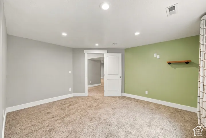 Interior room featuring neutral-tone carpeting, recessed ceiling lighting, a two-panel interior door, and a built-in wall shelf