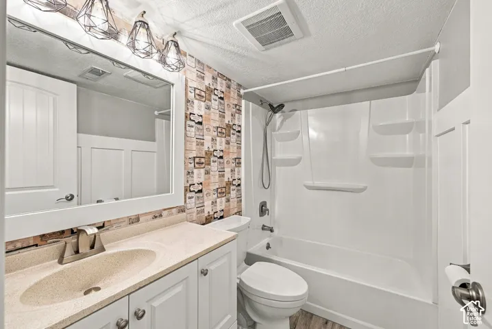Bathroom featuring white cabinetry, integrated sink, solid surface countertop, geometric metal light fixture, and tub-shower combination