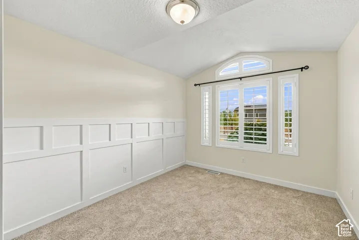Interior space featuring vaulted ceilings, white wainscoting, wall-to-wall carpeting, and a three-paneled window assembly with a semi-circular transom and plantation shutters