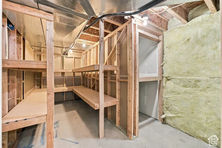 Unfinished storage area featuring exposed wood framing, built-in wooden shelving, fiberglass wall insulation, and concrete flooring