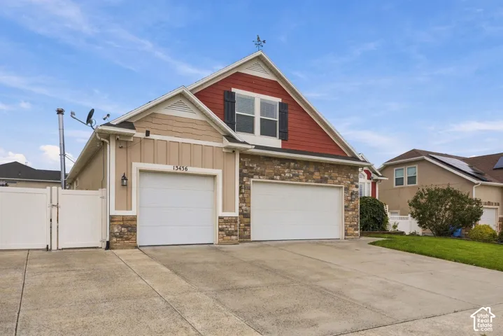 Multi-car garage exterior featuring mixed-material siding, decorative stone veneer, gabled roofline with a cupola, and white vinyl privacy fencing