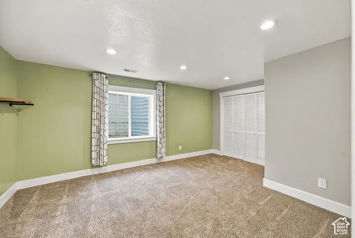 Room featuring neutral carpeting, recessed lighting, a sliding bifold closet with white doors, and a window with a corrugated metal window well