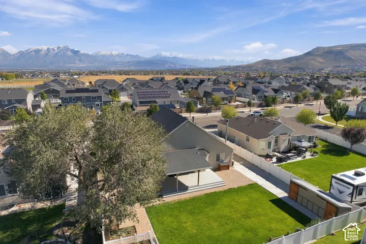 Aerial perspective featuring a covered backyard patio, mature landscaping, white vinyl perimeter fencing, and expansive mountain scenery