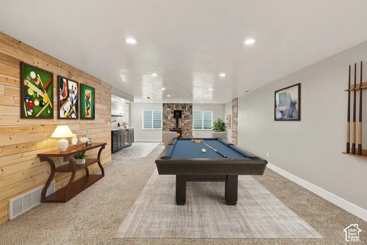 Natural wood plank accent wall, stone-surround wood-burning stove, wet bar with dark cabinetry, recessed lighting, and built-in cue rack