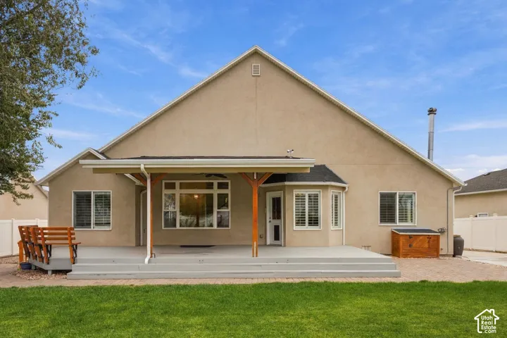 Stucco exterior featuring an expansive covered patio, raised tiered decking, a paved walkway, and a manicured lawn