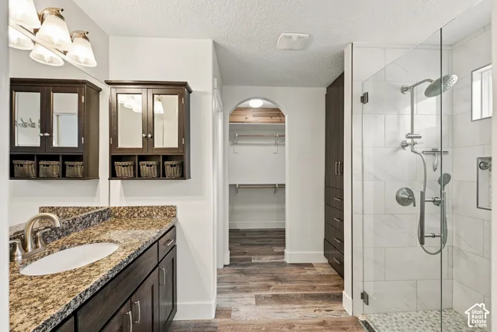 Bathroom featuring a stone-top vanity with built-in cabinetry, walk-in shower with tiled surround, and wood-finish flooring