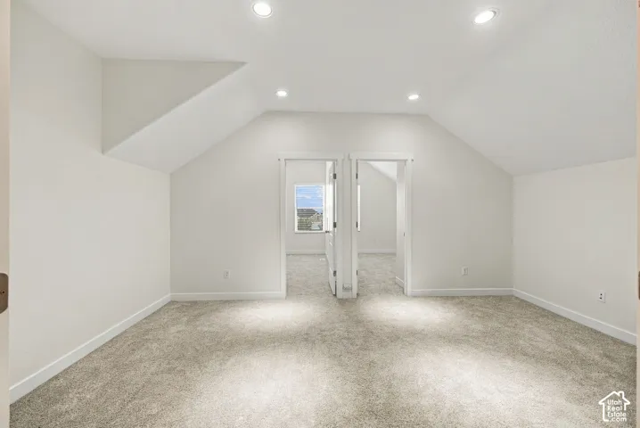 Vaulted ceilings, neutral carpeting, and recessed lighting