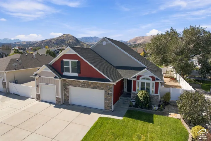 Multi-level exterior featuring stone veneer accents, multi-pane windows with shutters, a multi-car garage, and a manicured lawn set against a mountain backdrop