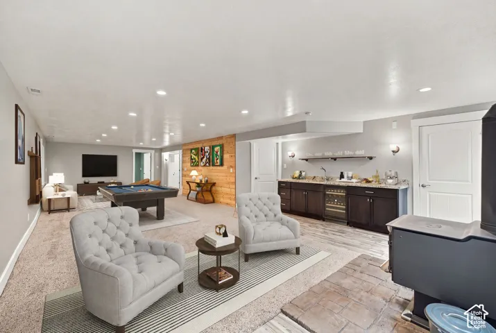 Finished interior space featuring recessed lighting, a wet bar with dark wood cabinetry and a stone countertop, a wood-accent wall, and a wood-burning stove on a stone hearth