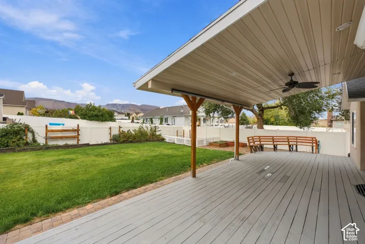 Covered deck with a ceiling fan, manicured lawn, perimeter vinyl fencing, and built-in wood seating