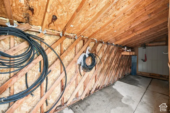 Storage area featuring exposed timber wall and roof framing, oriented strand board paneling, concrete flooring, and built-in wall-mounted shelving
