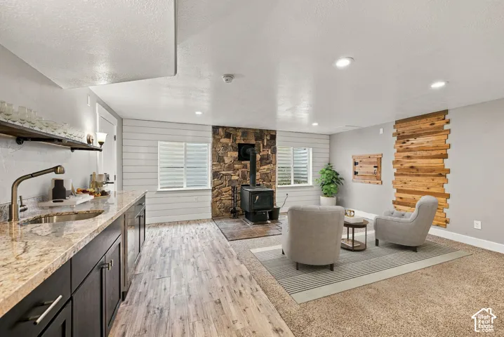 Kitchen area featuring dark cabinetry, stone-patterned countertops, and a wood-finish floor, complemented by a stone-surround wood-burning stove and a wood-slat wall feature