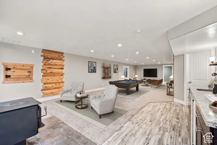 Open-concept area featuring a wood-plank accent wall, recessed lighting, wood-finish flooring, stone-tiled hearth, and a built-in wet bar with a solid surface countertop