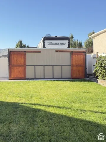 Outdoor shed featuring sliding wood doors, metal panel siding, and a concrete foundation, situated on a grass lawn with vinyl perimeter fencing