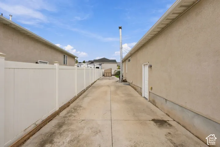 Concrete side yard with a white vinyl privacy fence and exterior wall-mounted light fixture