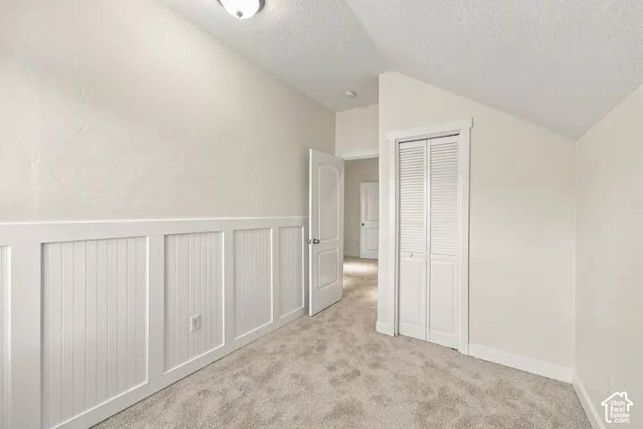 Room featuring a vaulted ceiling, wall-mounted board-and-batten wainscoting, neutral carpeting, and a closet with louvered double doors