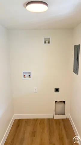 Dedicated utility space featuring wood-finish flooring, a flush-mount ceiling fixture, recessed plumbing hookups, an electrical panel, and dedicated dryer venting