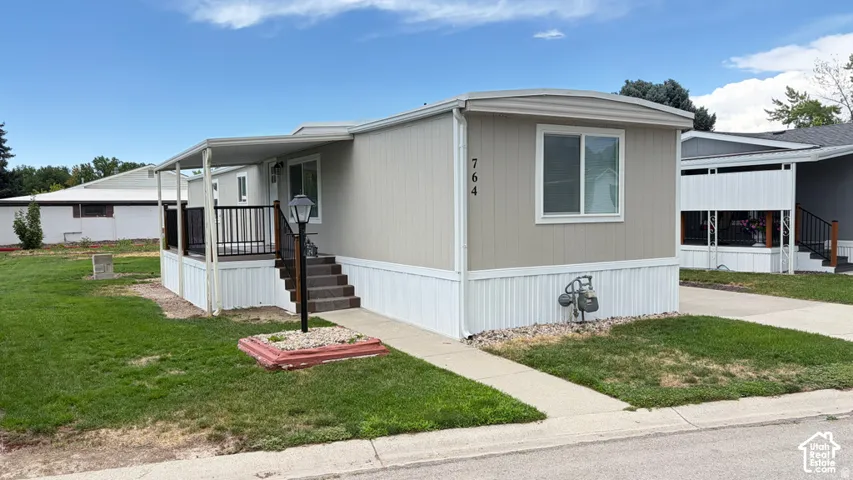 Neutral-toned exterior siding with white trim, covered front porch featuring metal railing, concrete walkway, and dedicated off-street parking area
