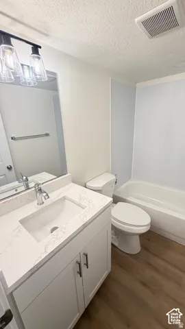 Bathroom featuring a white vanity with a stone-patterned countertop, an integrated rectangular sink, wood-finish flooring, and a tub-shower combination with full-height surround