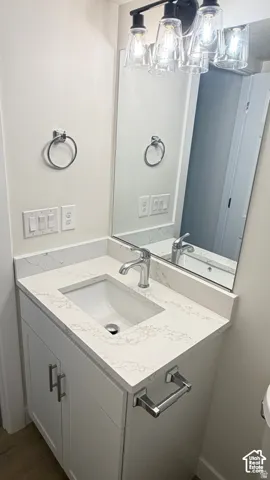 Bathroom vanity featuring a stone-composite countertop with integrated sink, polished chrome faucet, shaker-style cabinetry, and multi-bulb glass light fixture