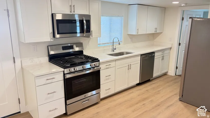 Kitchen featuring white shaker-style cabinetry, light-toned stone countertops, stainless steel appliances, and wood-finish flooring