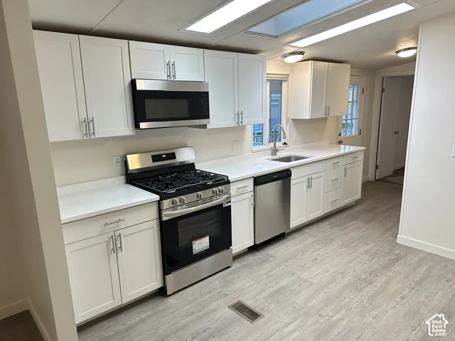 Kitchen featuring white cabinetry, stainless steel appliances, solid surface countertops, a dual-basin sink with a pull-down faucet, and wood-finish flooring