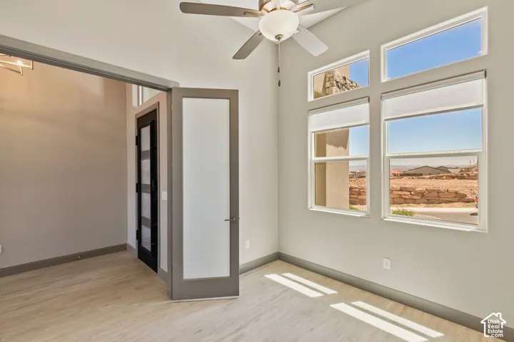 Room featuring high ceilings, wood-finish flooring, a ceiling fan with integrated lighting, frosted glass panel doors, and multiple windows with roller shades