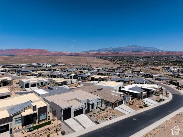 Aerial perspective of a residential neighborhood featuring modern single-story homes with stucco exteriors, flat rooflines, integrated two-car garages, and mountain backdrop