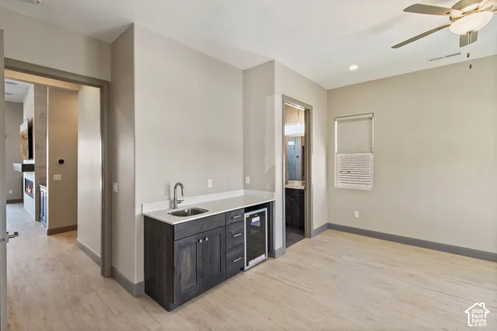 Wet bar featuring custom dark-toned cabinetry, light-toned stone-style countertops, an integrated beverage refrigerator, and a stainless steel sink with a high-arc faucet, set against wood-finish flooring