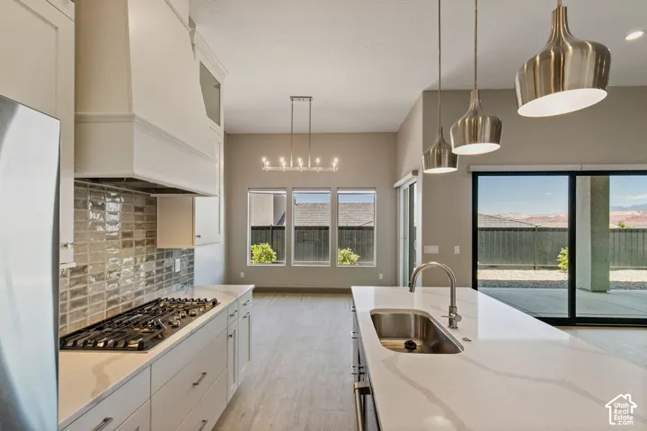 Kitchen featuring a large island with quartz countertops, custom white cabinetry, a gas cooktop with a tiled backsplash, and metallic pendant lighting