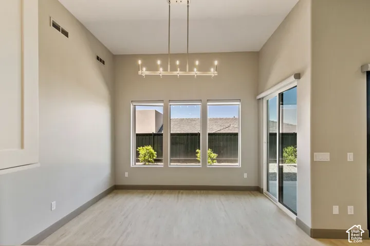 Vaulted ceiling featuring a linear metal chandelier, wood-finish flooring, and large windows with sliding glass door access to the exterior