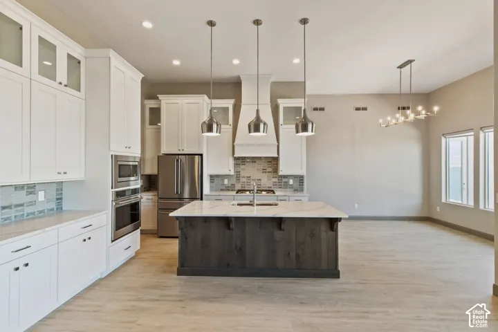 Kitchen featuring white cabinetry with glass-front uppers, a central island with a dark wood-finish base and light countertop, stainless steel double wall ovens, a tiled backsplash, and three pendant lights