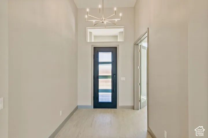 Entryway featuring vaulted ceilings, a modern multi-arm chandelier, an exterior door with horizontal glass panels, a rectangular transom window, and wood-finish flooring