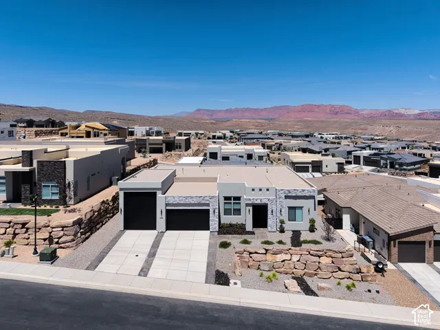 Contemporary exterior featuring stone veneer accents, a flat roofline, attached multi-car garage, and terraced rock retaining walls with desert-inspired landscaping