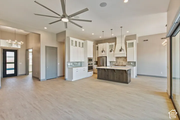 Open-concept kitchen featuring an expansive center island with stone countertop, white cabinetry with glass-paneled upper doors, stainless steel wall ovens, and recessed lighting